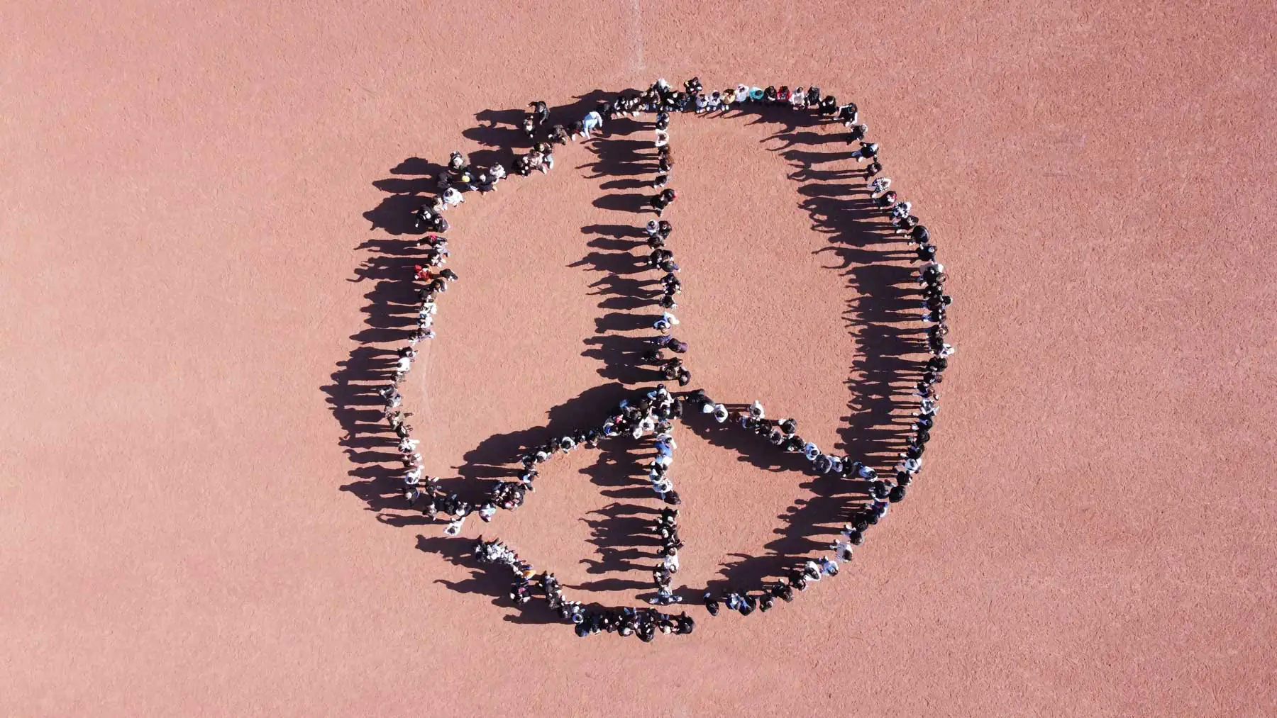 Schülerinnen und Schüler stellen sich in Peace-Zeichen-Form auf dem Schulhof auf