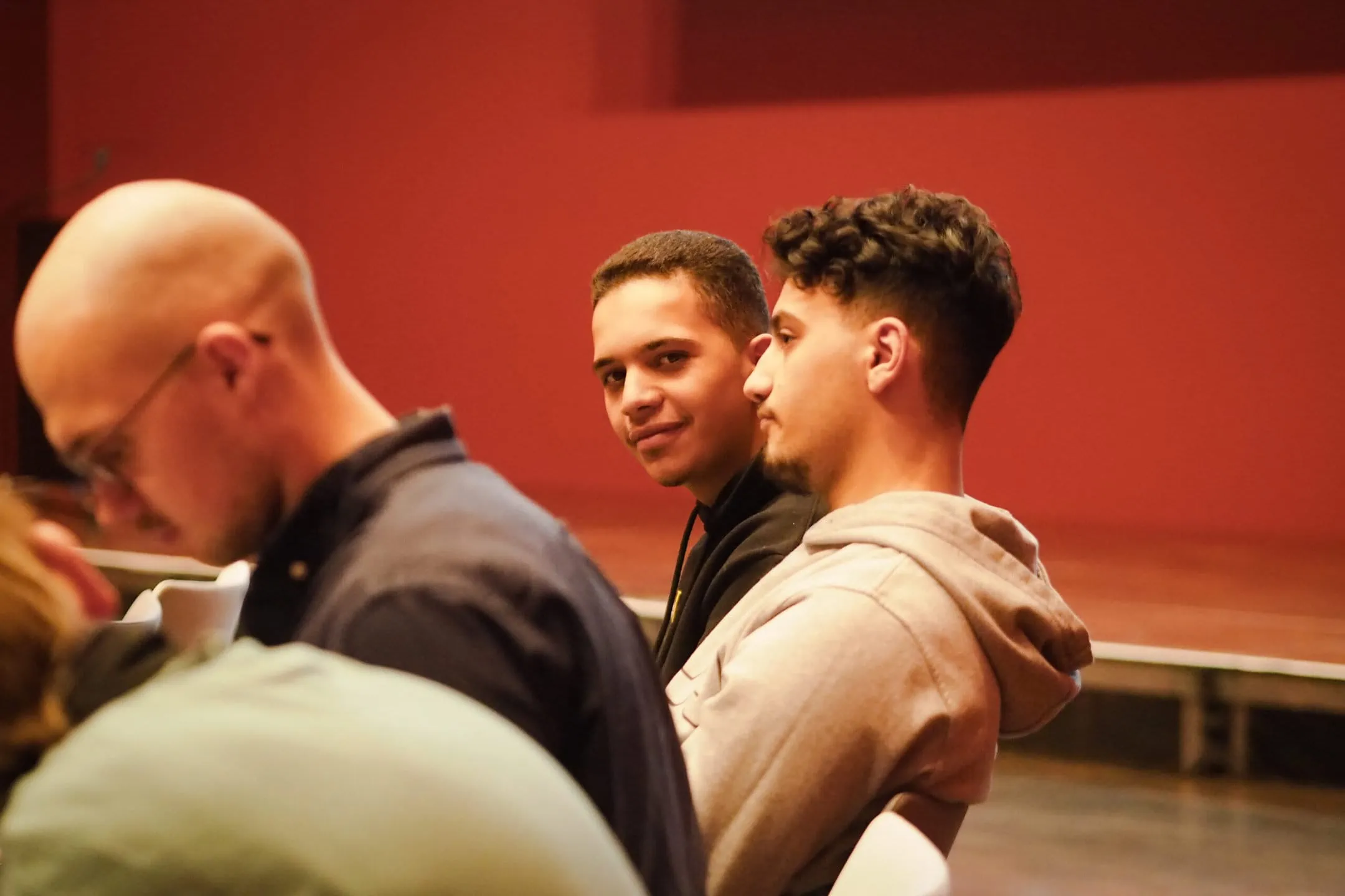 Ein Schüler im Publikum lehnt sich nach vorne und schaut an seinem Sitznachbarn vorbei in die Kamera