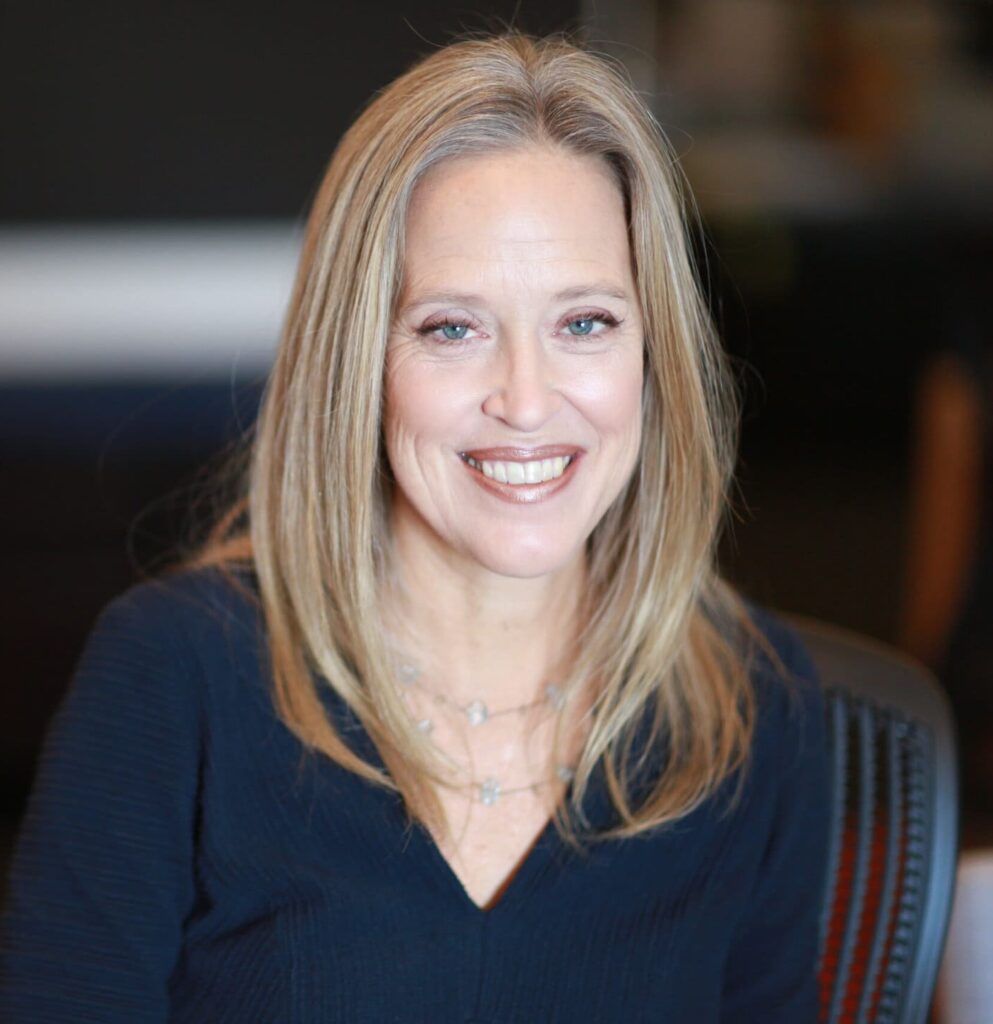 Portraitfoto von der offen lächelnden Wendy Kopp vor unscharfem Hintergrund