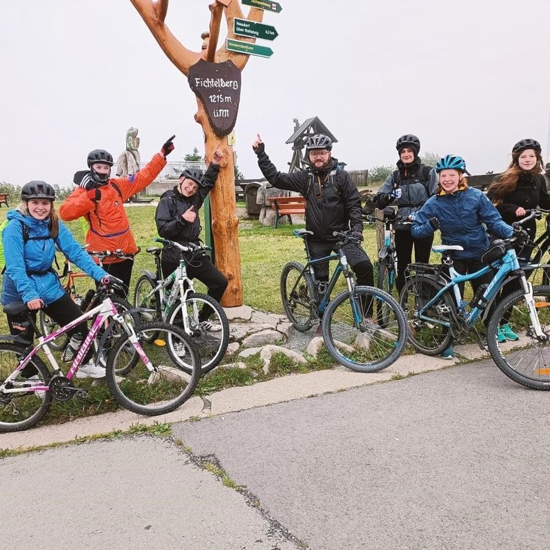 Gruppenfoto der Fahrer:innen, die mit ihren Rädern an einem Wegweiser posieren und darauf zeigen.